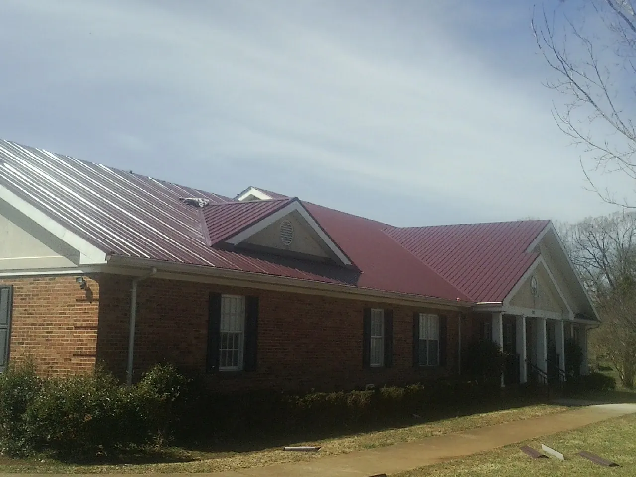 Red metal roof with gabled entries on a long brick building, from a Hail Damage Roof Repair job in Francisco