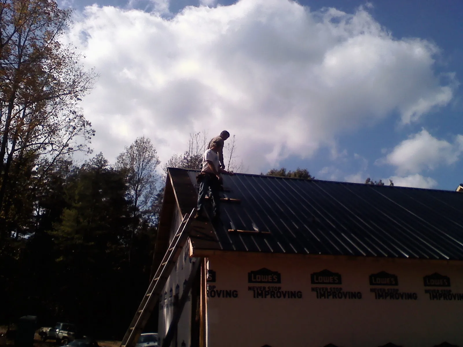 Roofer fastening dark metal panels high against a cloudy sky, from a Roof Inspection job in Francisco