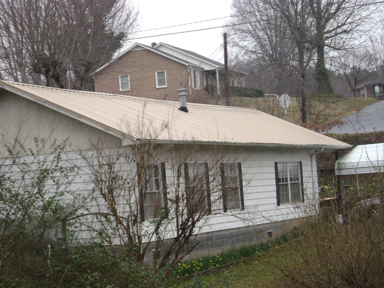 Tan metal roof on a white sided house set into a hillside — Commercial Roofing by Roofing Brothers in Francisco